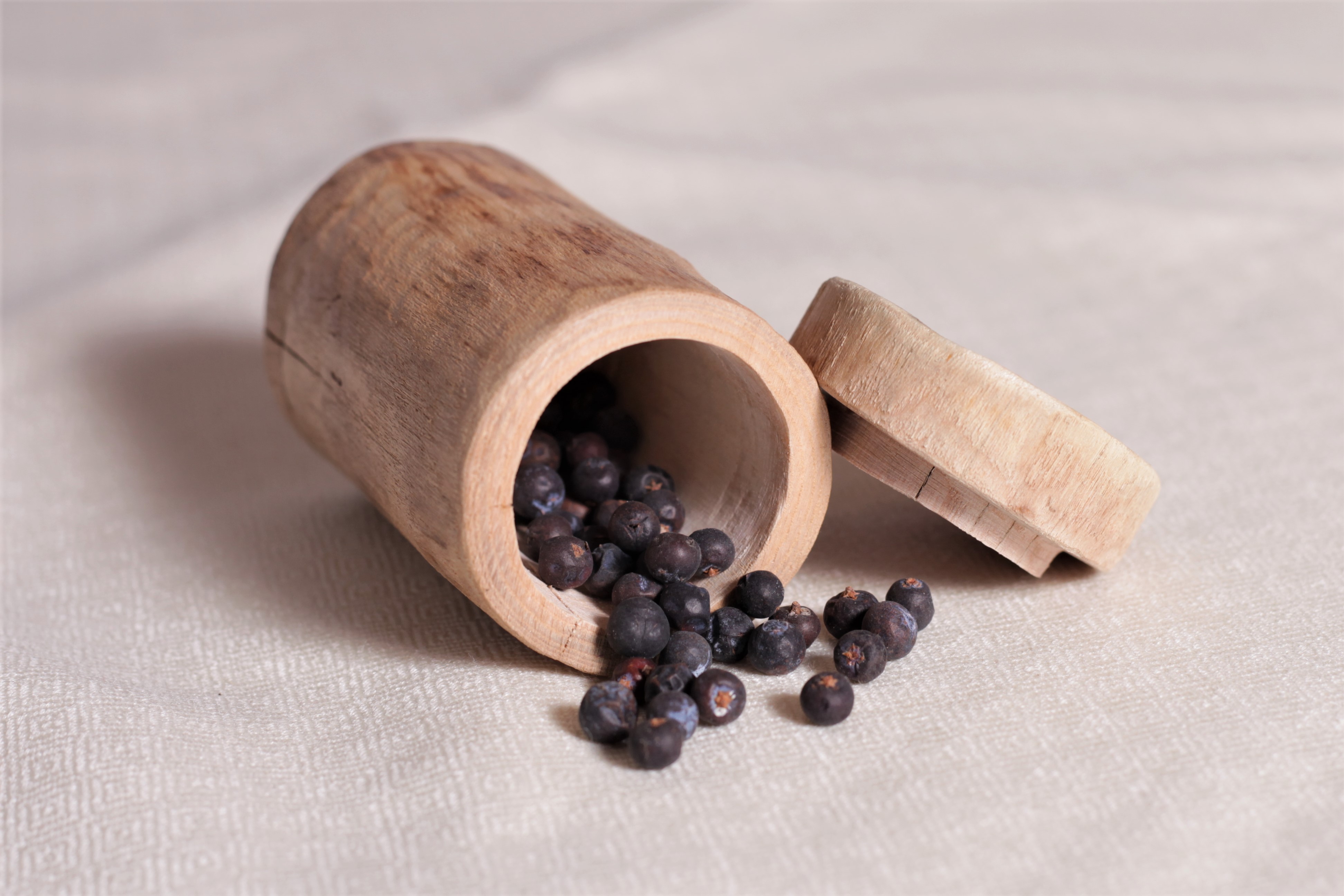Holzdose liegend mit herausrollenden Wacholderbeeren.